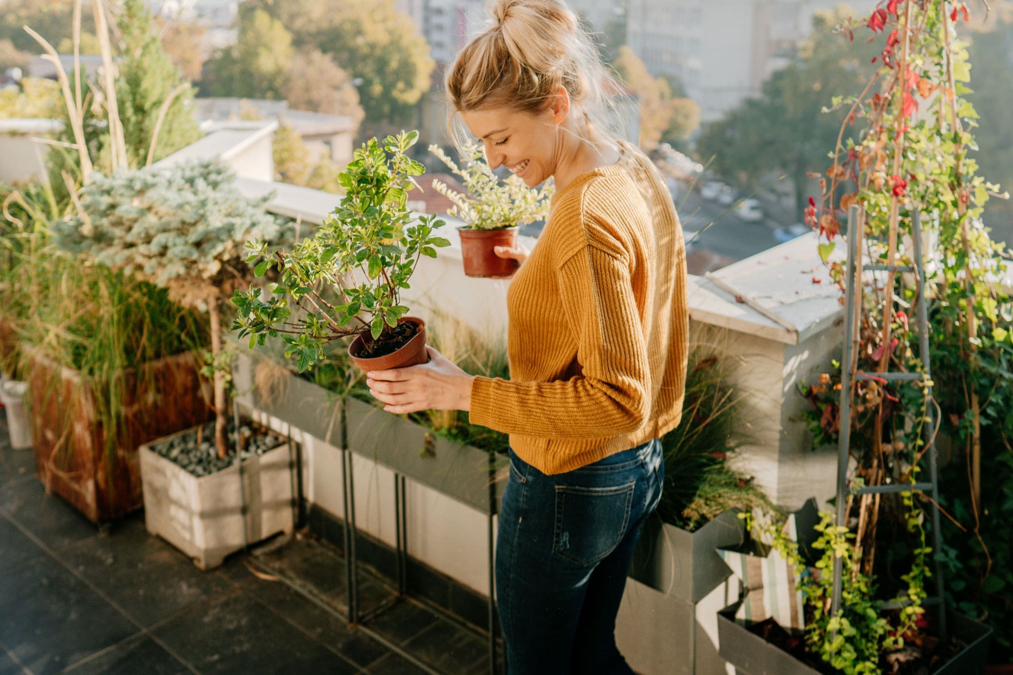 Una mujer feliz sosteniendo dos jarrones. En el fondo hay muchas plantas y flores.