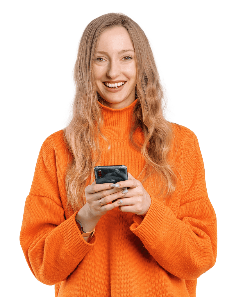 Una mujer con el pelo rubio está de pie en un fondo transparente. Lleva un gran jersey naranja y sostiene su teléfono.